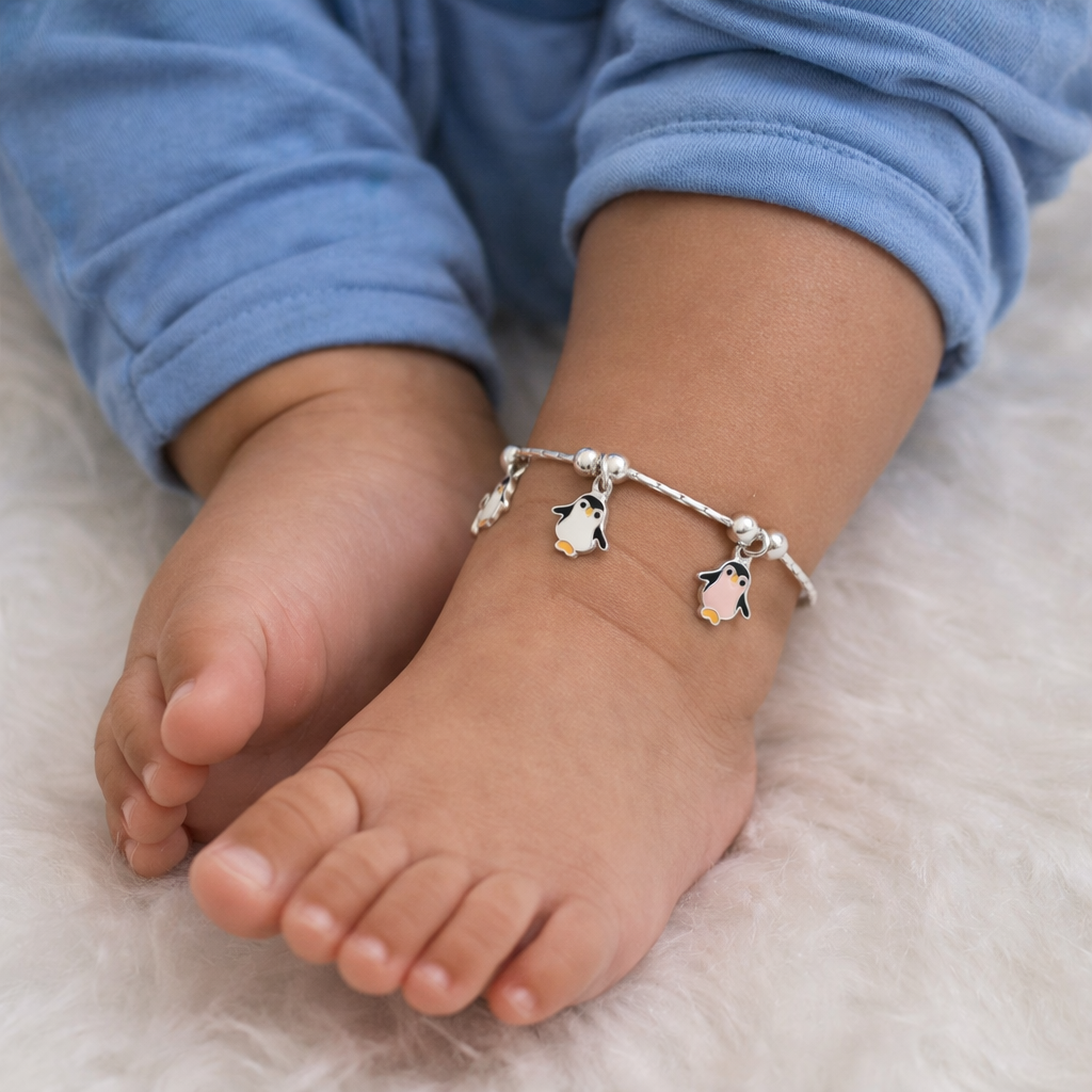 Child's foot wearing a silver anklet with penguin charms on a soft surface