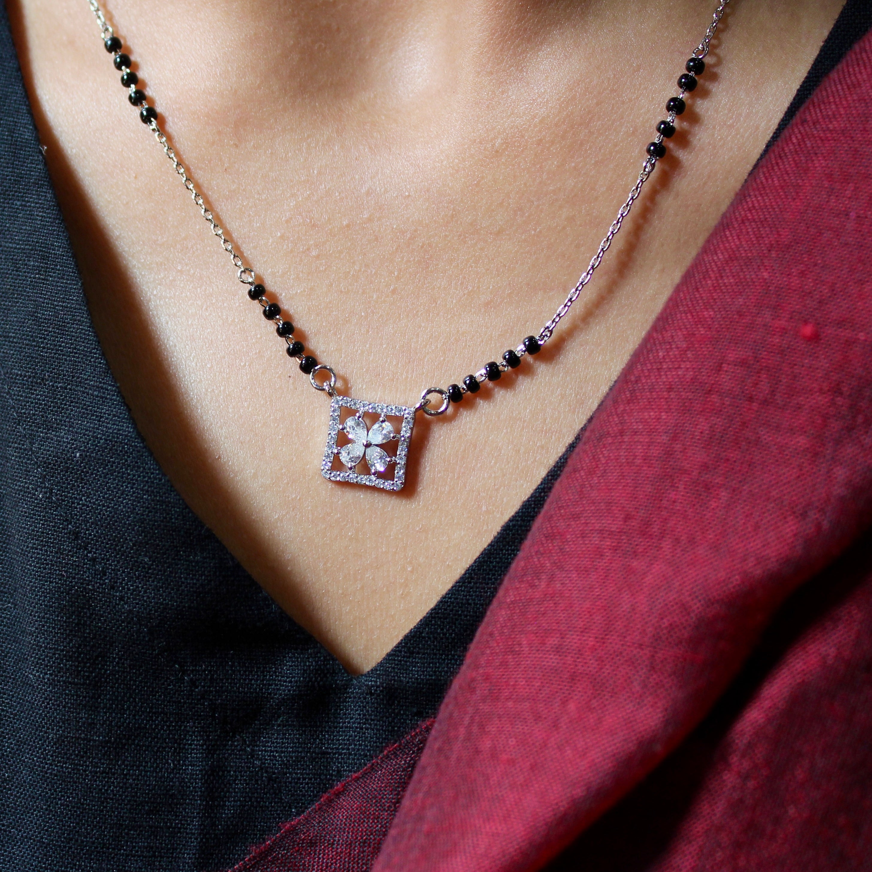 Necklace with a square pendant worn by a person in a black and red outfit.
