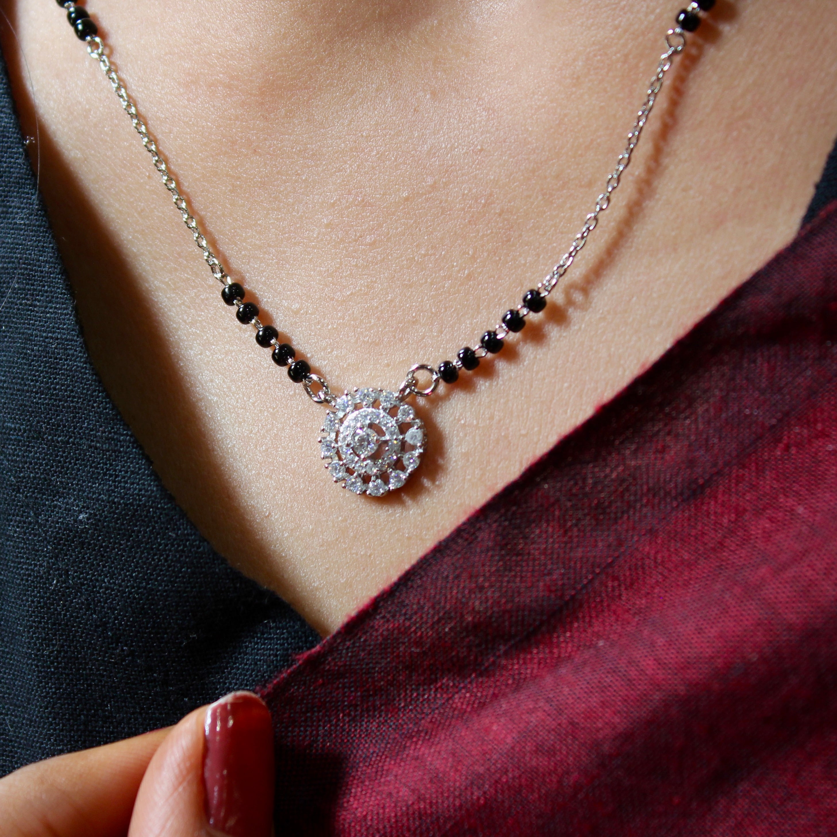 Necklace with a circular pendant and black beads on a person wearing a dark top and red fabric.