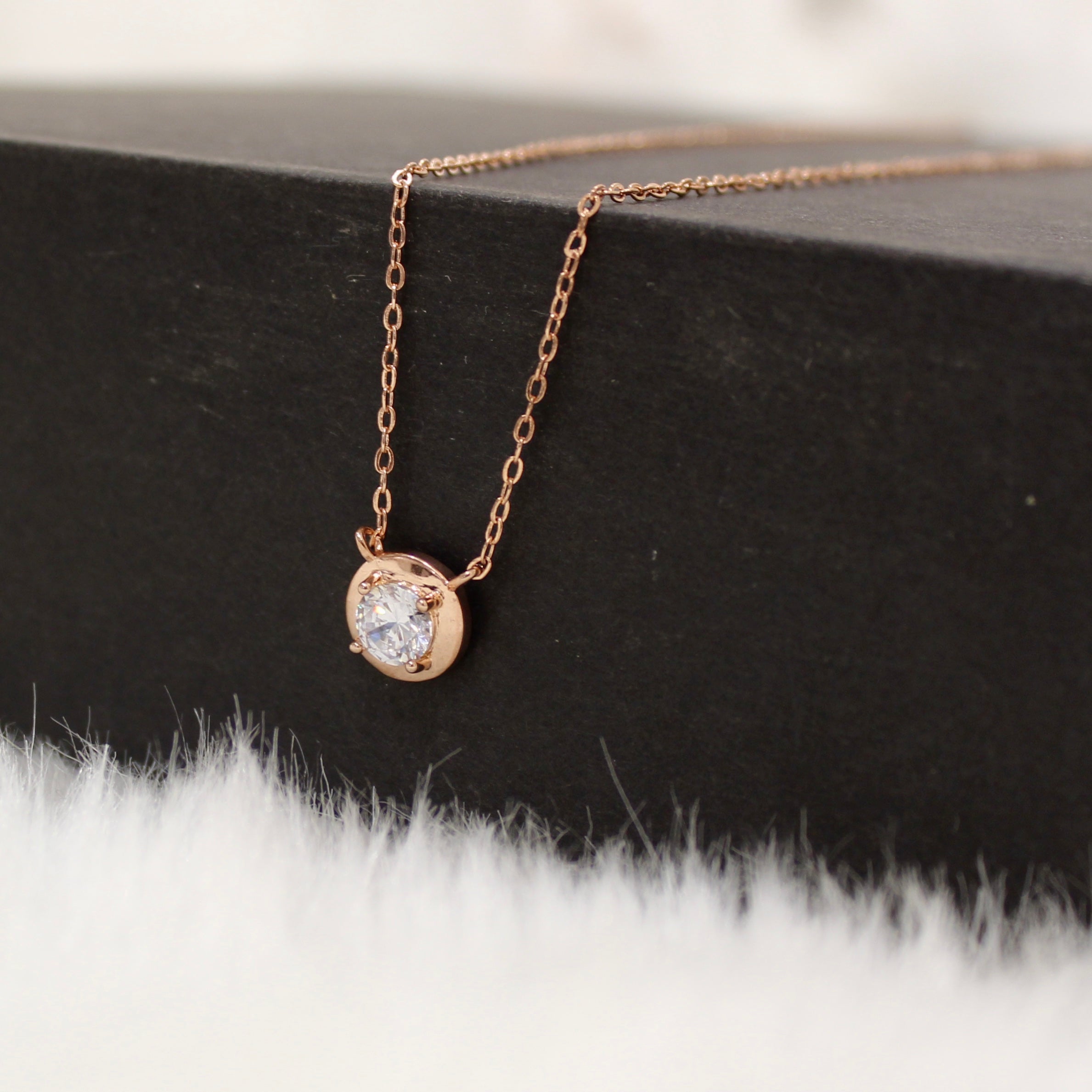 Rose gold necklace with a round diamond pendant on a white background