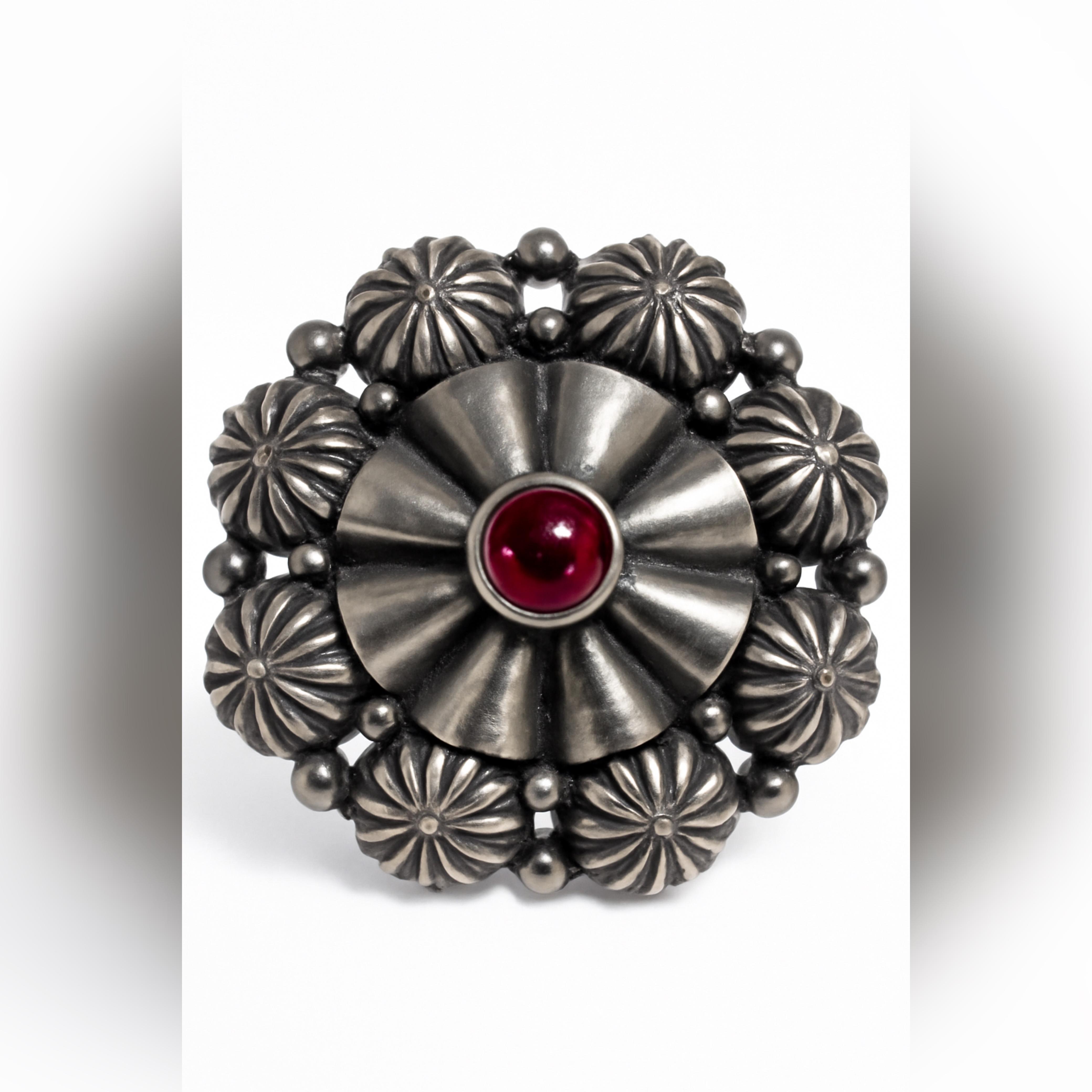 Silver brooch with a red central gemstone on a white background