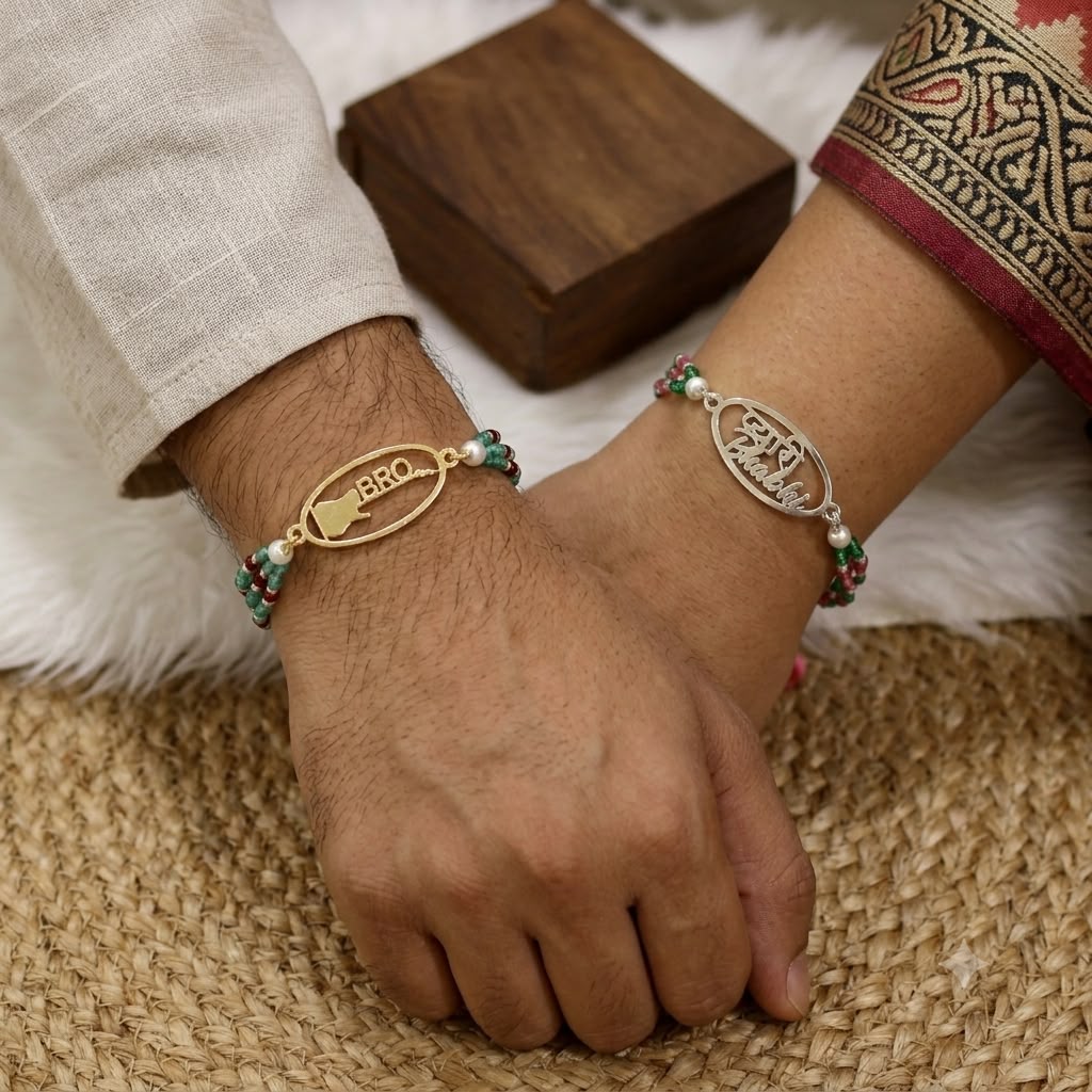 Two personalized bracelets worn on a couple's wrists, resting on their hands. One bracelet is gold-plated with a central oval charm engraved with 'BRO' and a small map of Kerala, accented with green and red beads.